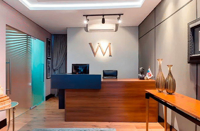 Recepção elegante do escritório Vargas Mildemberg Advogados Associados com balcão de madeira logo VM iluminado e decoração sofisticada representando advogado plano de saúde empresarial quando contratar