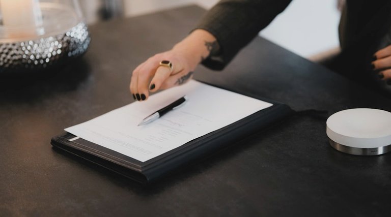 Mão sobre documento em mesa de trabalho durante análise de legitimidade em transação imobiliária
