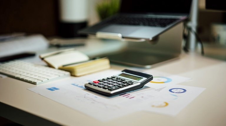 Calculadora sobre documentos financeiros e notebook em mesa de trabalho para cálculo de indenização por atraso