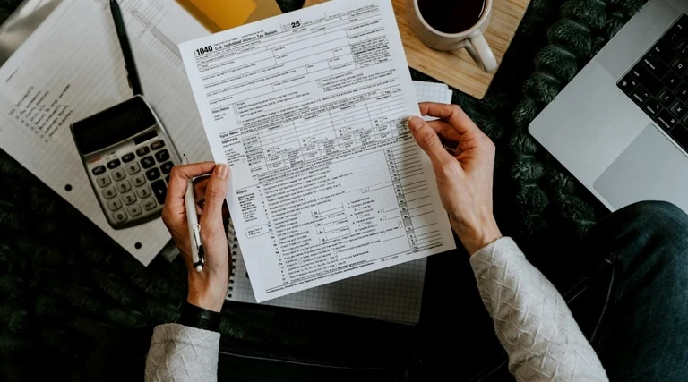 Pessoa analisa formulário de IPTU e calculadora sobre mesa, representando autuações fiscais em imóvel sem habite-se
