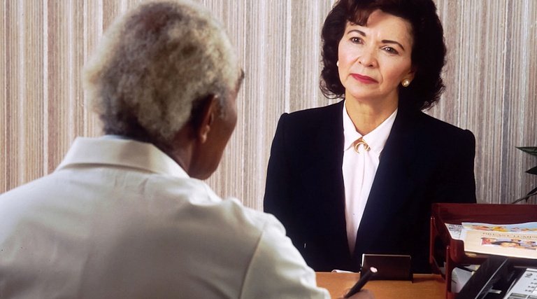 Conversa sobre atraso na entrega de apartamento Atraso na entrega de apartamento: profissional de terno conversando com pessoa sentada em escritório
