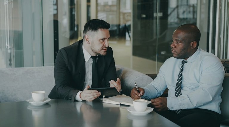 Reunião profissional sobre atraso entrega imovel na planta Atraso entrega imovel na planta: dois homens de terno conversando em mesa com cadernos e xícaras de café
