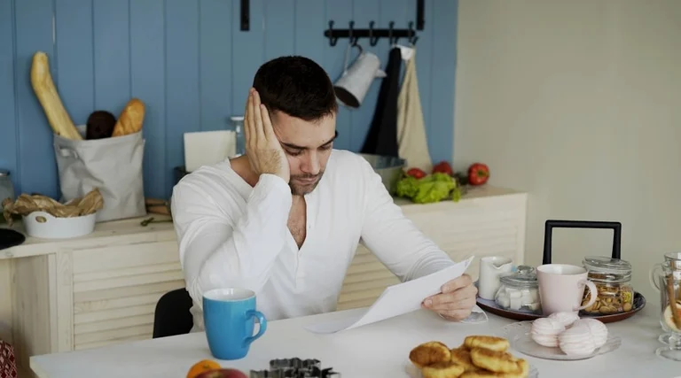 Imóvel quitado e não entregue: erros contratuais analisados imóvel quitado e não entregue: Pessoa preocupada analisa documentos imobiliários à mesa demonstrando erros contratuais