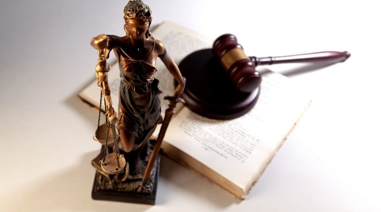 Estátua da Justiça com balança ao lado de martelo e livro jurídico representando processos de imposto de herança