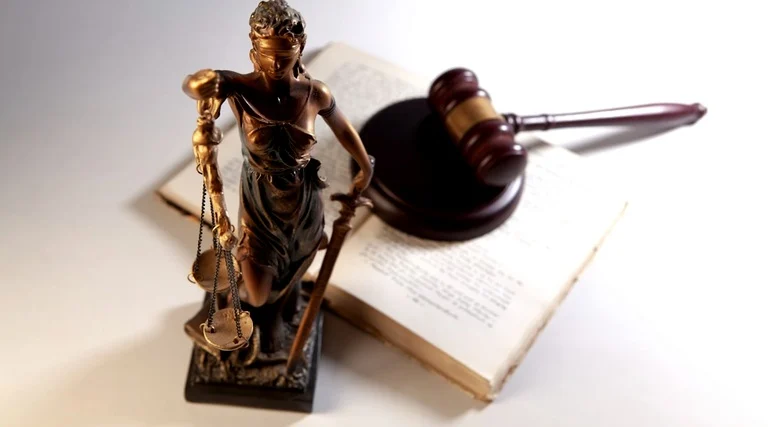 Estátua da Justiça com balança ao lado de martelo e livro jurídico representando processos de imposto de herança