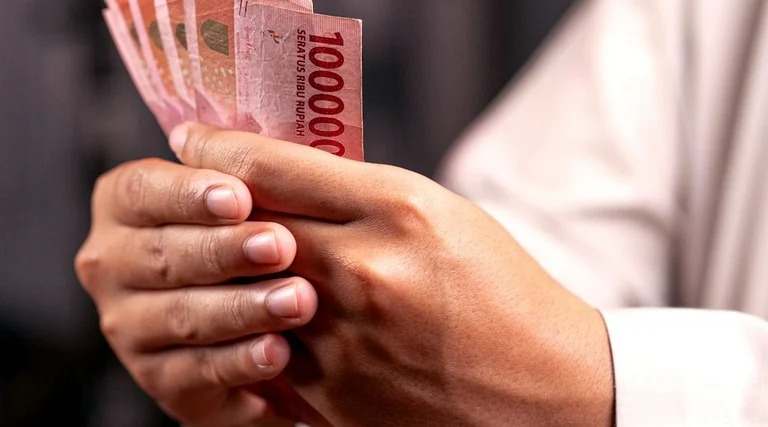 holding patrimonial vantagens e desvantagens: Pessoa segura notas de dinheiro avaliando decisões financeiras